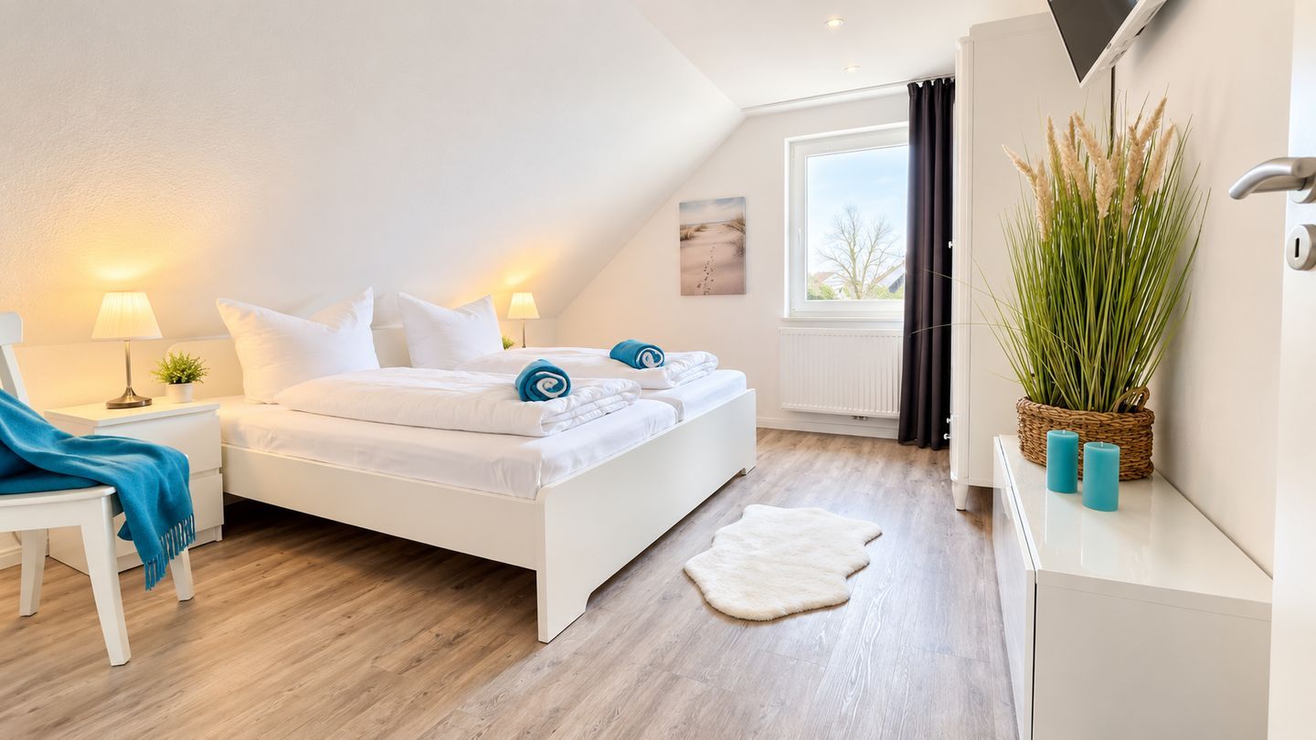 Un dormitorio moderno con cama blanca, una mesita de noche, una lámpara, una planta y vistas al exterior.