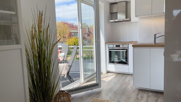 A modern kitchen with a built-in oven, a large window with a view of the outside, and a sliding glass door leading to a balcony.