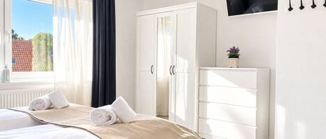 Een hotelkamer met een bed, een kledingkast, een televisie en een raam met gordijnen.