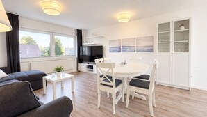 Una sala de estar moderna con un sofá, una mesa de comedor con sillas, un televisor y una zona de cocina con armarios.
