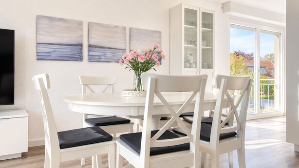 Un comedor con mobiliario blanco, un televisor de pantalla plana y obras de arte en la pared.