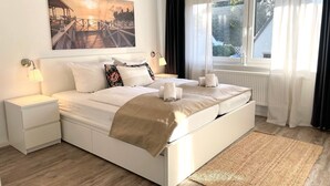 A bedroom with a bed, bedside tables, a window with curtains, and a painting on the wall.