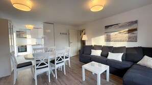 A modern living room with a black sofa, white dining table, and chairs, a small white coffee table, and a painting on the wall.