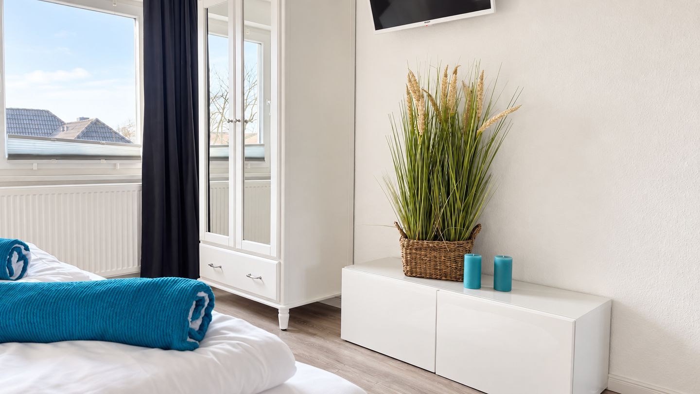 Een hotelkamer met een bed, een witte ladekast, een aan de muur bevestigde televisie en een raam met uitzicht op gebouwen.