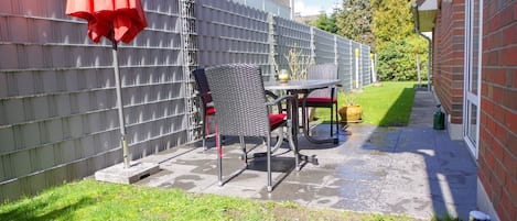 Un patio con una mesa, sillas y una sombrilla roja, junto a una pared de ladrillo.