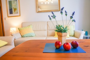 A living room with a wooden coffee table, a sofa, a potted plant, and a framed picture on the wall.