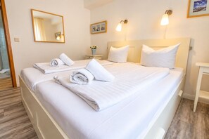 Habitación de hotel con dos camas, ropa blanca, un espejo, luces fijadas en la pared y una mesita de noche pequeña.