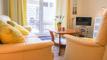 Ein modernes Wohnzimmer mit einer Couch, einem Sessel und einem kleinen Tisch mit Pflanze und Obst.
