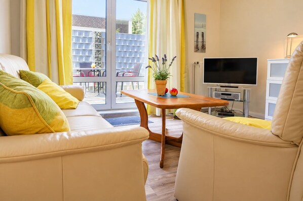 Una sala de estar moderna con un sofá, sillones, una mesa de centro, un televisor y un balcón con cortinas amarillas.