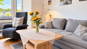Una sala de estar moderna con un sofá gris, una mesa de centro de madera, un sillón gris y un jarrón con flores.
