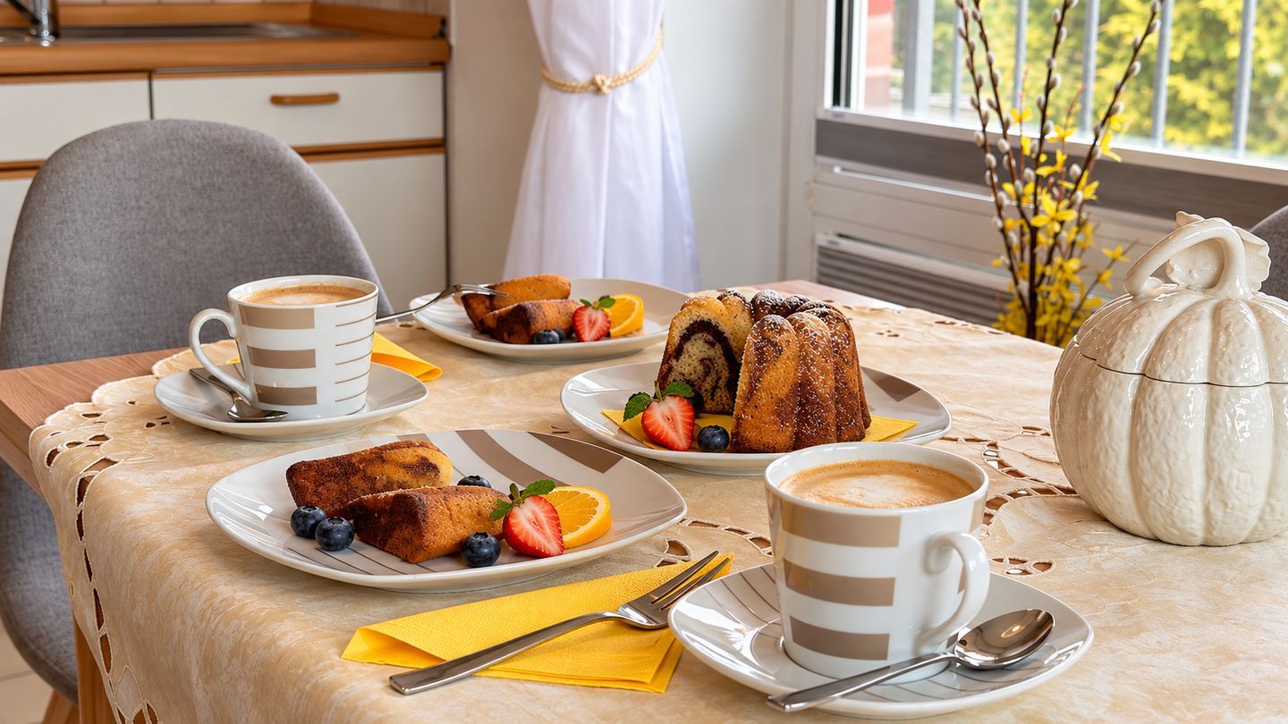 A breakfast setting with plates of food, coffee cups, and a decorative vase.