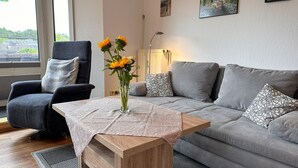 A living room with a grey sofa, a black armchair, a wooden coffee table, and a vase with flowers.