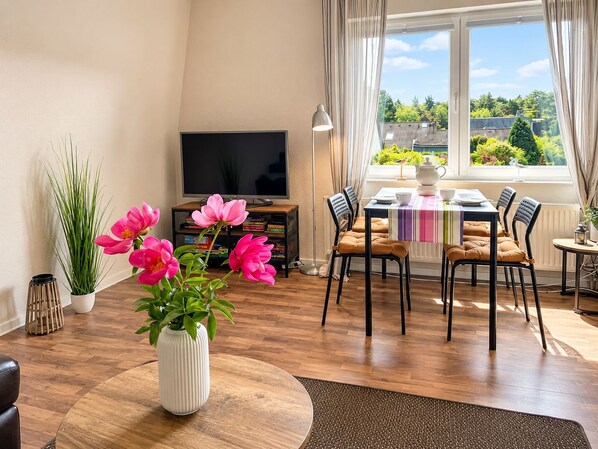 Una sala de estar con televisor, mesa de comedor, sillas y vistas al exterior.