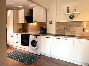 A modern kitchen with white cabinetry, a built-in oven, a washing machine, a coffee maker, and a sink.