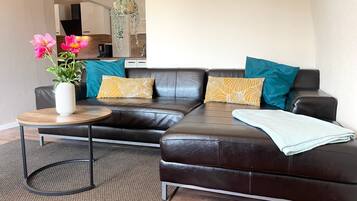 A modern living room with a leather sofa, a round wooden coffee table, a vase with flowers, and a hanging plant.