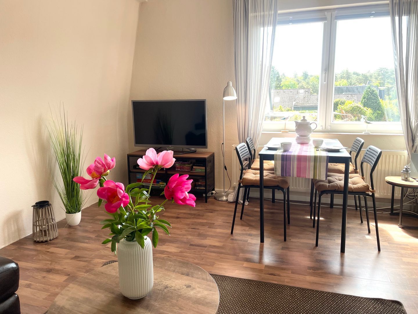 Een woonkamer met een televisie, eettafel, stoelen, een salontafel, een kamerplant en een raam met gordijnen.