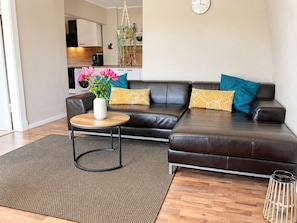 A modern living room with a brown leather sofa, a round wooden coffee table, and a potted plant with pink flowers. - NO6 - Ferienwohnung mit Gemütlicher Ausstattung, 5 Min. zum Strand - Nige Ooge (Cuxhaven)
