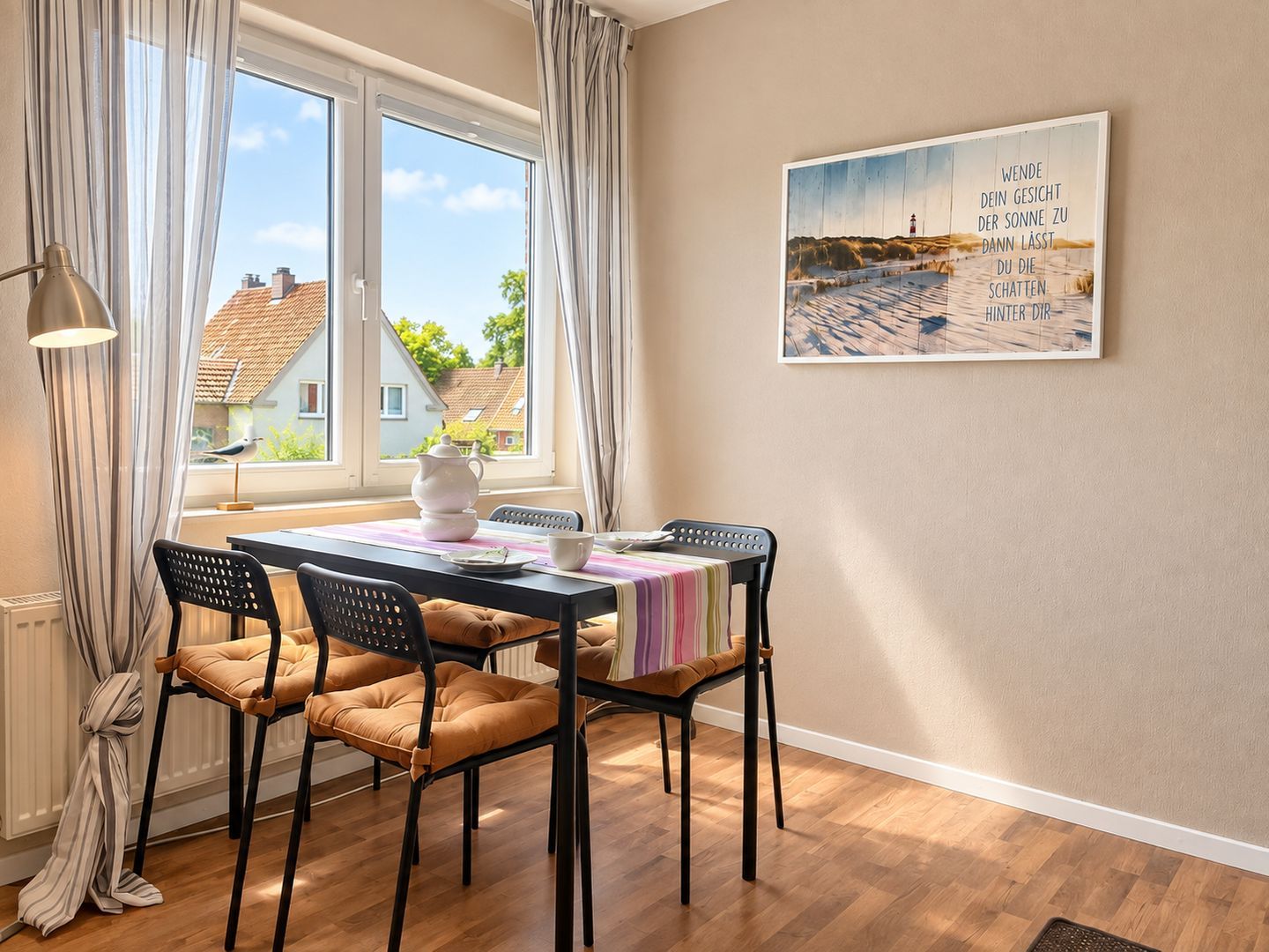 Comedor con mesa dispuesta para cuatro personas, sillas, una ventana con cortinas y un cuadro colgado en la pared.