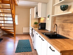 Una cocina moderna con encimeras de madera, lavadora integrada, cafetera y escalera de madera.