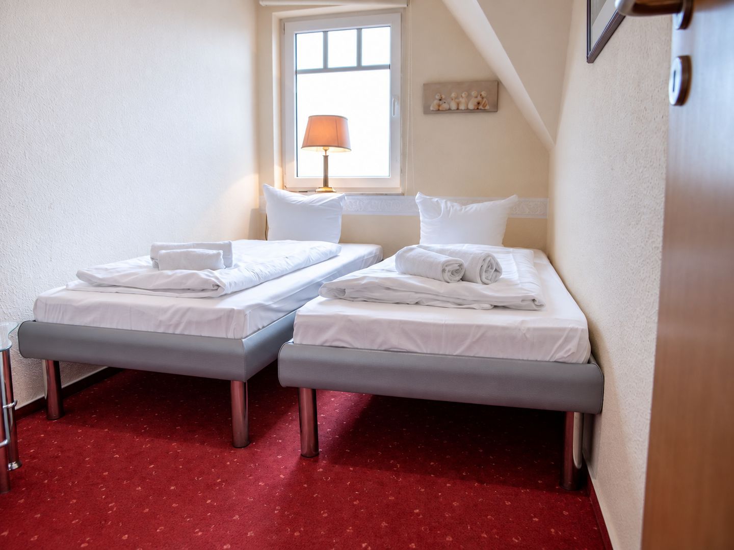 Ein Hotelzimmer mit zwei Einzelbetten, einem Fenster mit Lampe und einem roten Teppich.