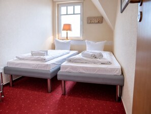 Una habitación de hotel con dos camas individuales, una ventana con lámpara y una alfombra roja.