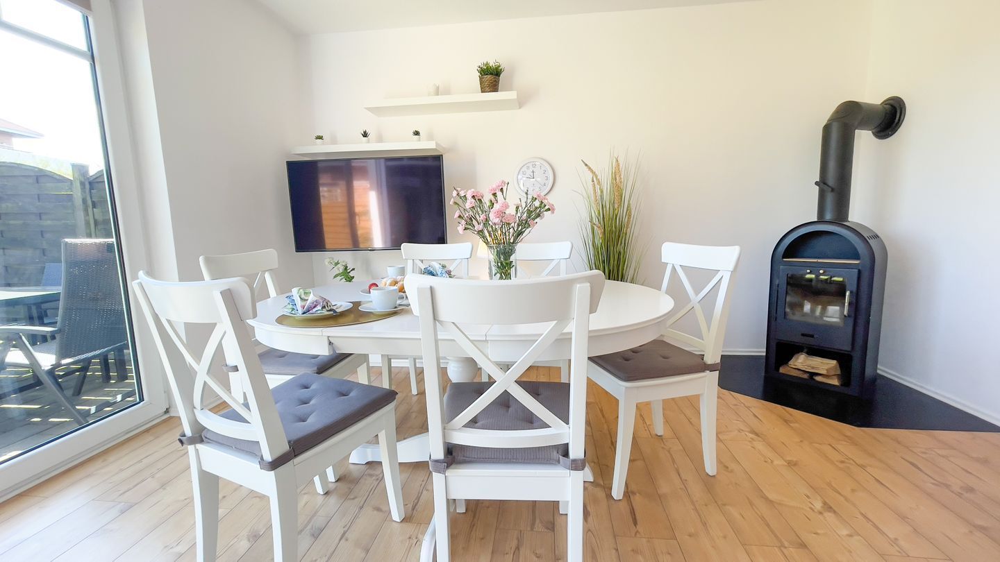 A dining area with a round table, white chairs, a TV, and a black wood stove.