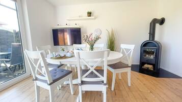 A dining area with a round table, white chairs, a TV, and a black wood stove.