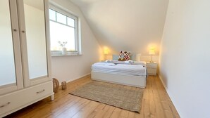 A bedroom with a bed, bedside lamps, a window, a wardrobe, and a floor lamp.
