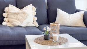 A modern living room with a grey sofa, a white throw pillow, a decorative woven basket, a small potted plant, and a glass candle holder.