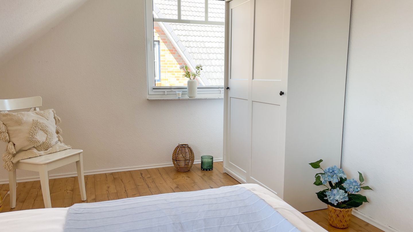 A bedroom with a bed, a chair, a window with a view of a building, and a door.