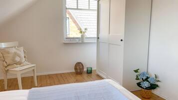 A bedroom with a bed, a chair, a window with a view of a building, and a door.