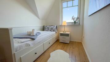 Een slaapkamer met een bed, nachtkastje, lamp, raam en uitzicht op de lucht.