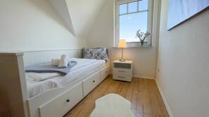 A bedroom with a bed, bedside table, lamp, window, and a view of the sky.