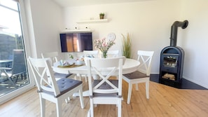 A dining area with a round table, white chairs, a TV, and a black wood stove.
