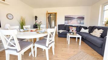 Un salon avec une table ronde blanche, un canapé gris et un tableau représentant un lac.