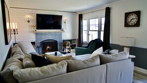 A living room with a fireplace, a sofa, a television, and a clock on the wall. - 5 minute walk to beach, walk to town & train (Fairfield)