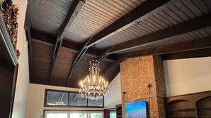 A spacious living area with a fireplace, a large TV mounted on a brick wall, and a chandelier. - Welcome to The Urban Mansion in Midtown Tallahassee (Tallahassee)