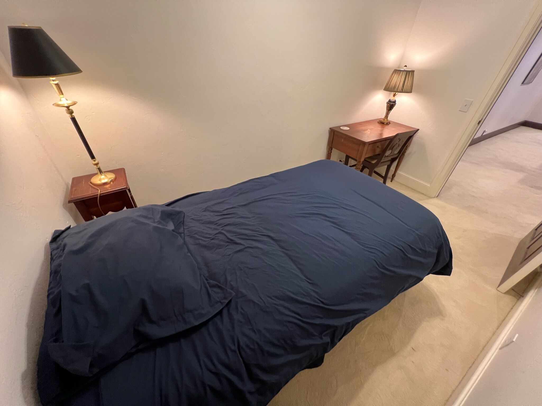 A bedroom with a bed, a nightstand, a desk, and a chair.