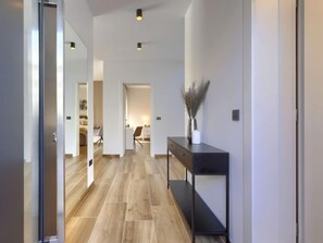 A modern hallway with wooden flooring, a black console table with a vase, and a mirror on the left.