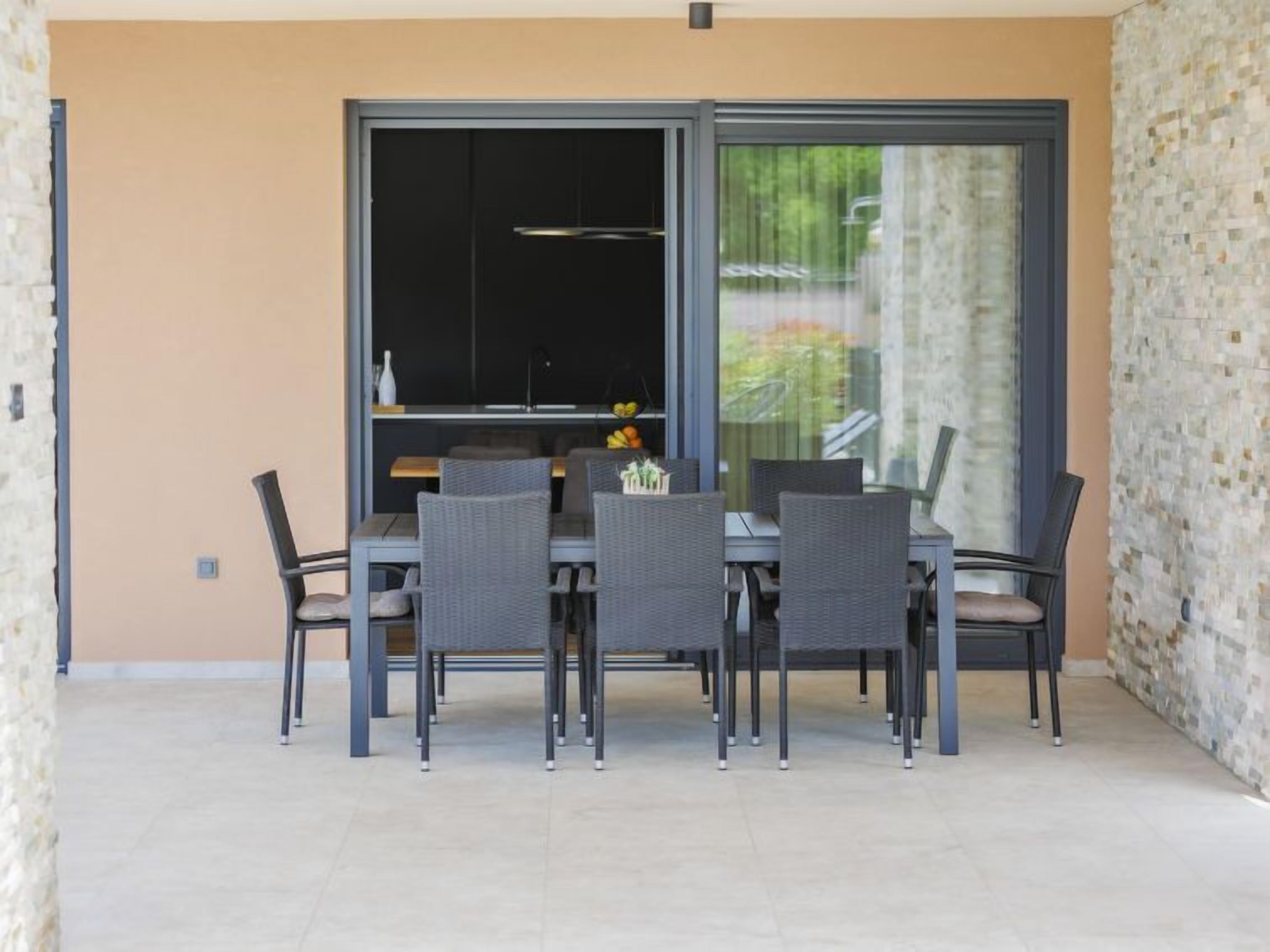 Un área de comedor al aire libre con mesa y sillas, un ventanal corredero y vistas de vegetación.