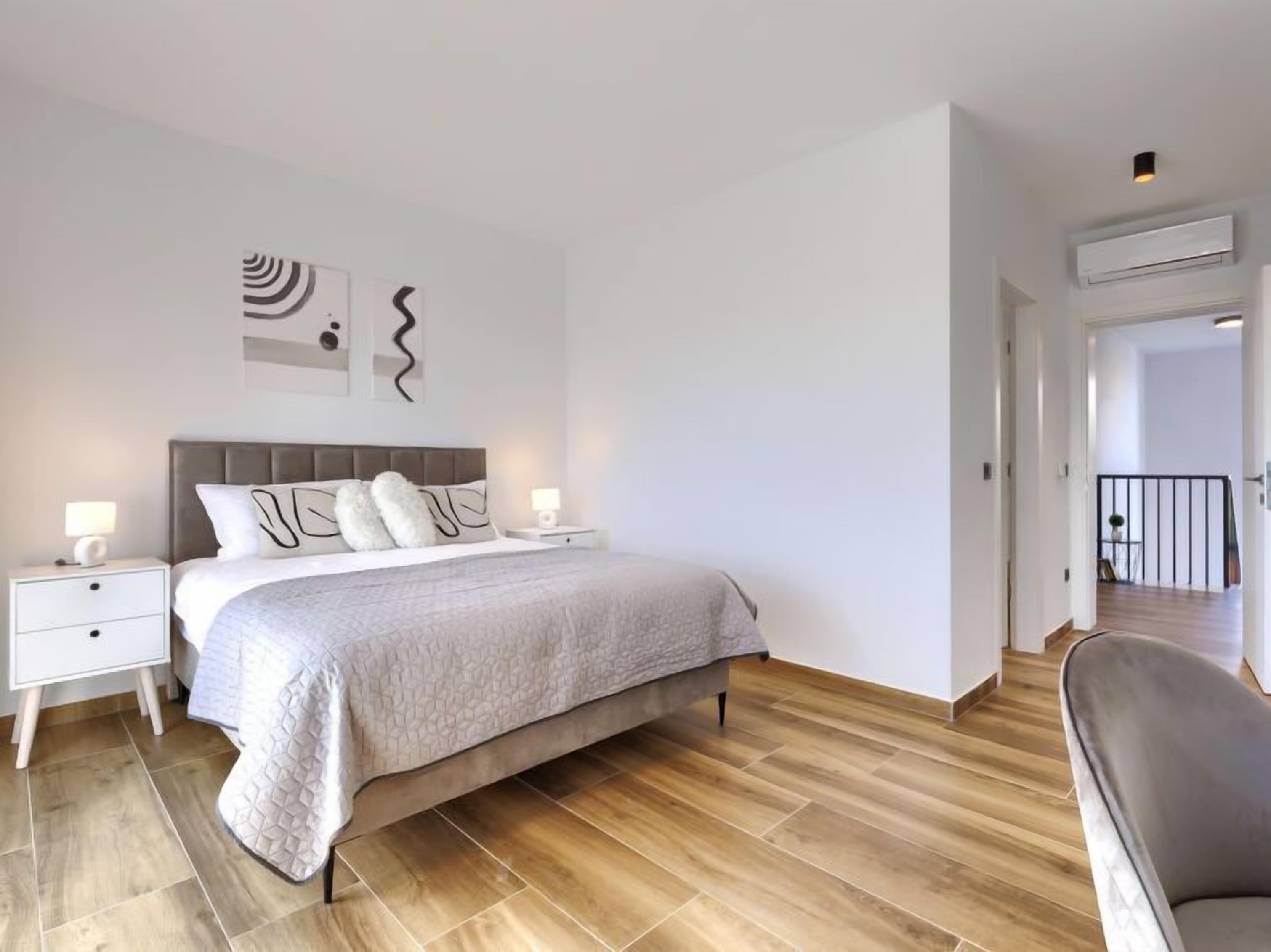 Een moderne slaapkamer met een groot bed, twee nachtkastjes met lampen en uitzicht op de gang.