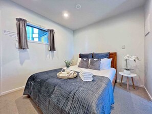 A bedroom with a bed, a bedside table with a plant, a window with curtains, and a small round table. - Ponsonby View 1-Bedroom with Pool in the City Centre (Auckland)