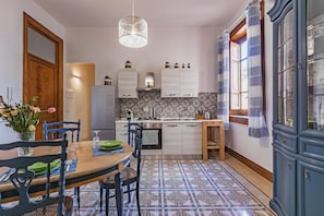 A kitchen with a dining table, chairs, a hanging light fixture, cabinets, and a patterned floor.