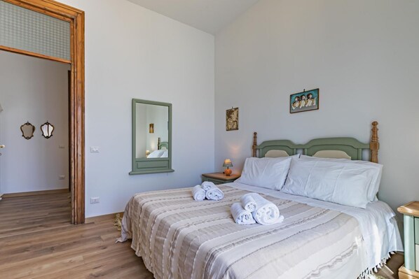A bedroom with a bed, a nightstand, a mirror, and artwork on the wall.
