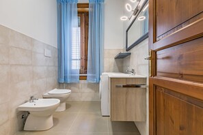 A bathroom with two toilets, a bidet, a washing machine, and a wooden cabinet.