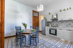 A kitchen with a dining table, chairs, a refrigerator, cabinets, and a patterned floor.