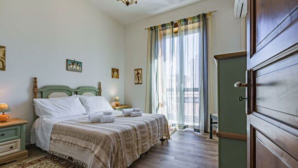 Ein Schlafzimmer mit einem Bett, Nachttischen, einem Schminktisch und einem Fenster mit Vorhängen.