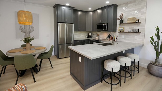 A modern kitchen with grey cabinets, stainless steel appliances, a central island with stools, and a dining area with green chairs. - Trendy & Oh-So Contemporary (Scottsdale)