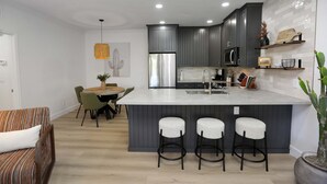 A modern kitchen with grey cabinets, a stainless steel refrigerator, and a central island with bar stools. - Trendy & Oh-So Contemporary (Scottsdale)