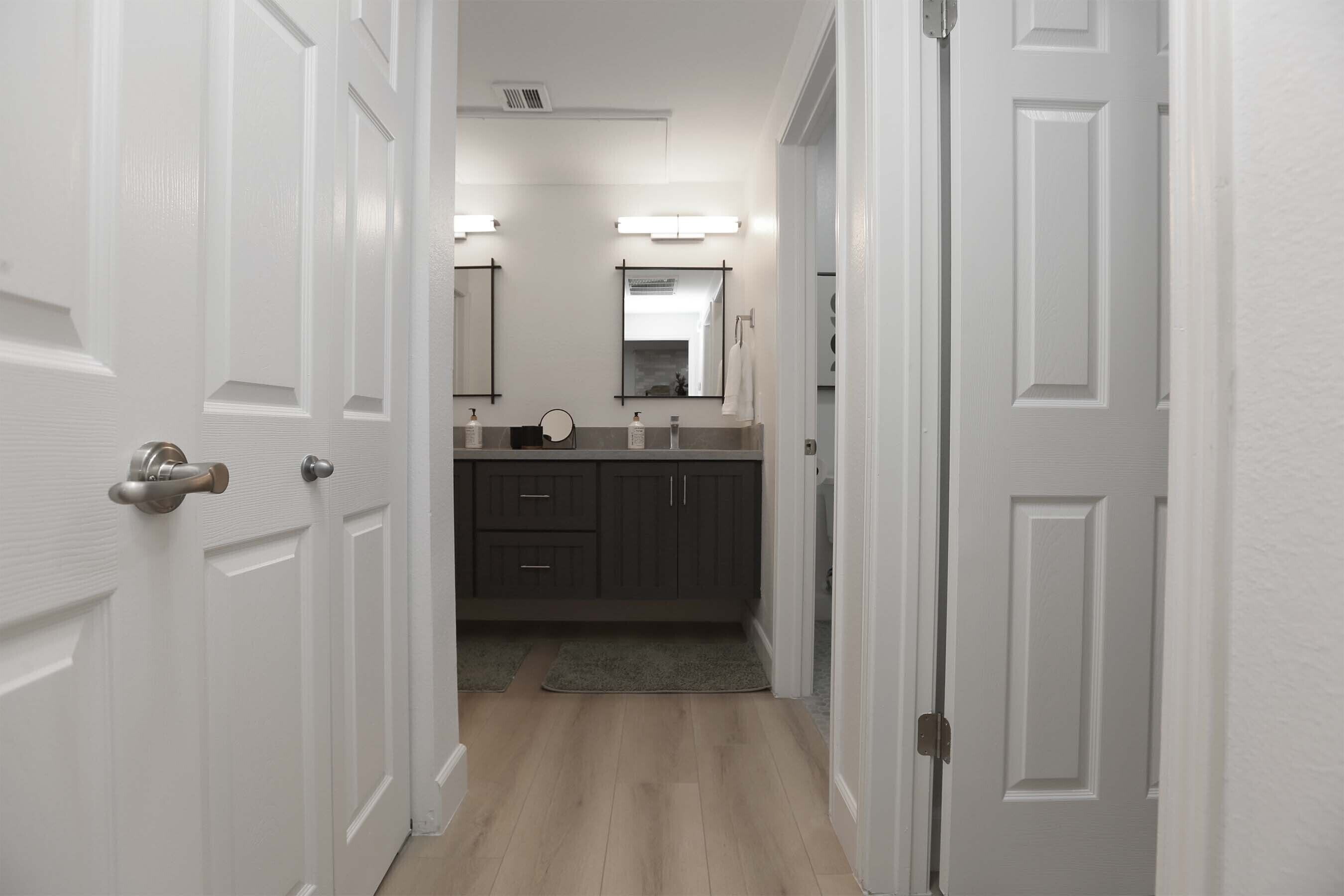 A hallway leading to a bathroom with a vanity, mirror, and towel rack.